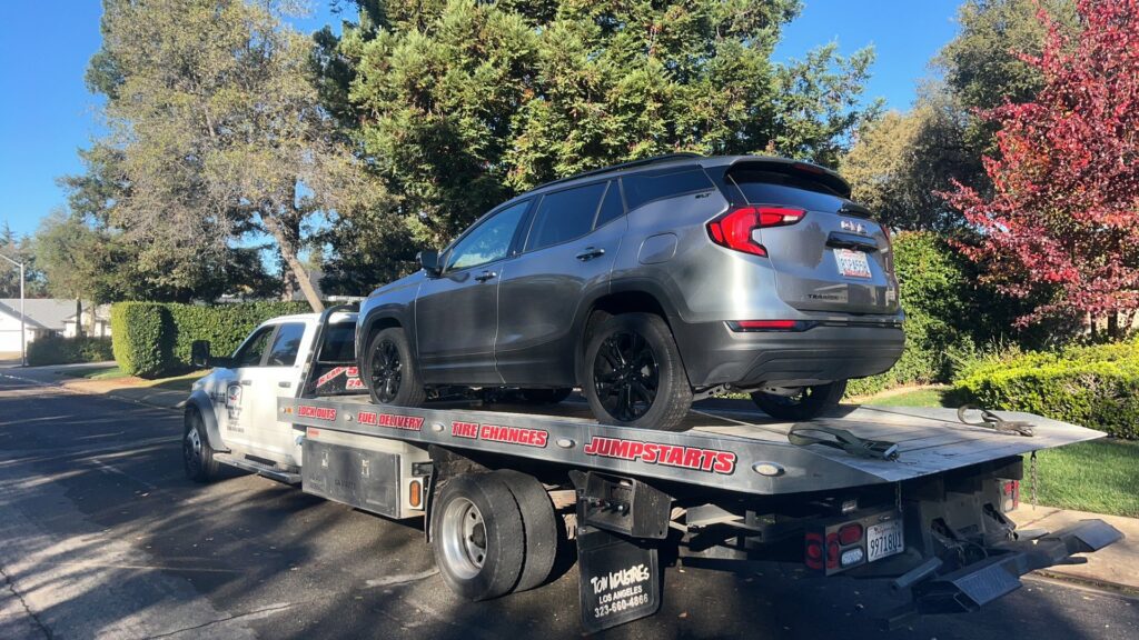 A white flatbed tow truck from Kennedy Towing & Transport in Anderson, CA, transporting a grey SUV on a sunny day.