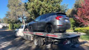 A white flatbed tow truck from Kennedy Towing & Transport in Anderson, CA, transporting a grey SUV on a sunny day.