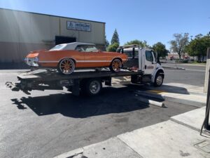 A white flatbed tow truck from Anthony's Towing & Transportation transporting an orange classic car in Yuba City, CA.