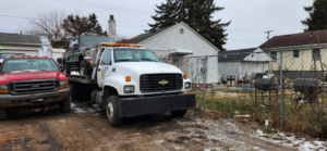 A white flatbed tow truck transporting a dark pickup truck for Boyz Automotive & Towing in Toledo, OH.