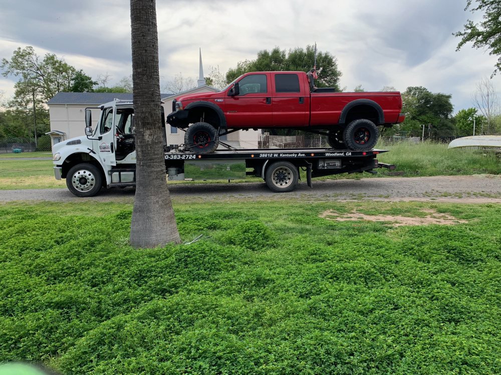A white flatbed tow truck from Anthony's Towing & Transportation transporting a red lifted pickup truck in Yuba City, CA.