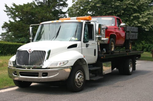 A white flatbed tow truck transporting a red pickup truck for Towing Services Of Omaha in Omaha, NE.