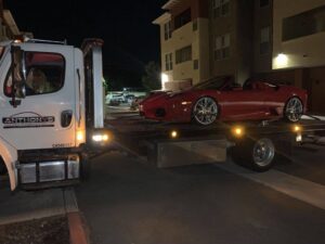 A white flatbed tow truck from Anthony's Towing & Transportation transporting a red sports car at night in Yuba City, CA.