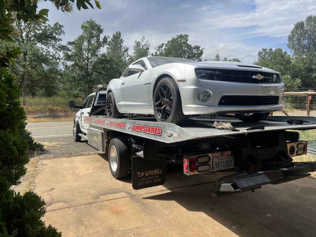 A white flatbed tow truck from Kennedy Towing & Transport in Anderson, CA, transporting a silver Chevrolet Camaro.