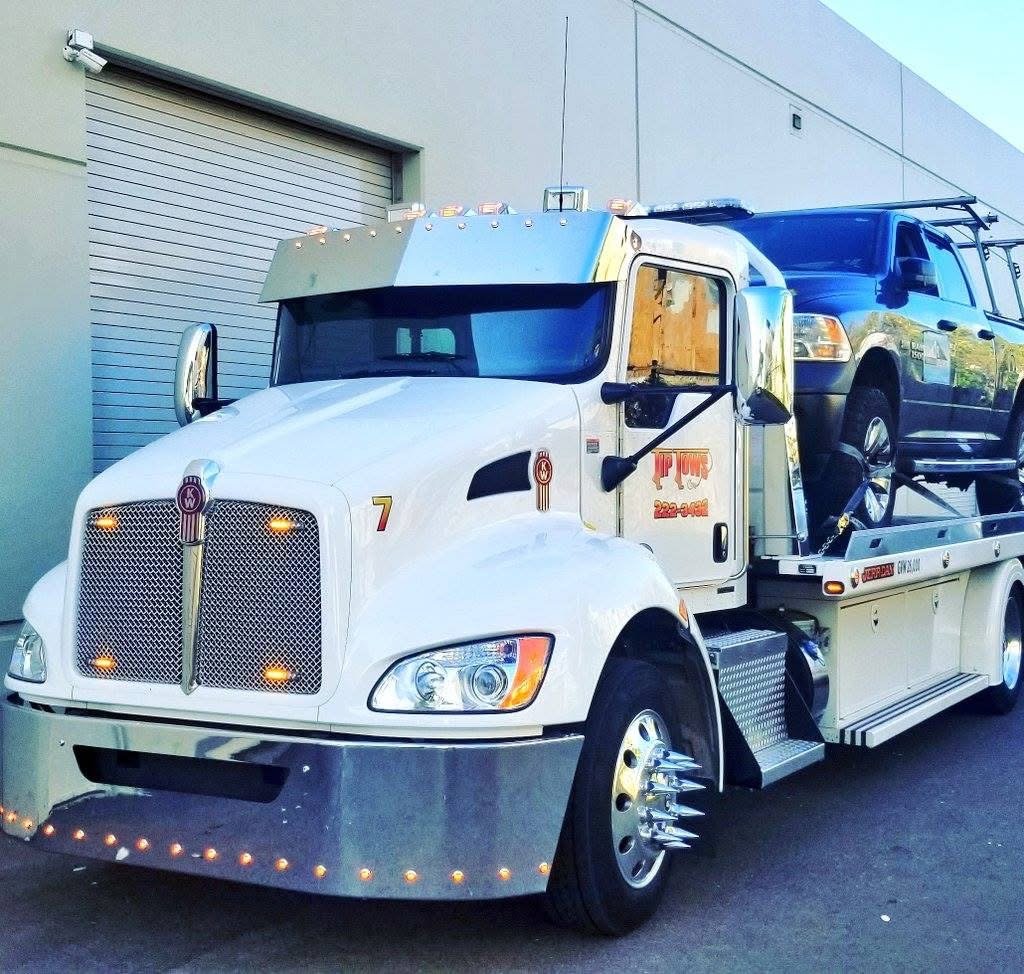 A white Tip Tows flatbed tow truck transporting a dark SUV in Honolulu, HI.