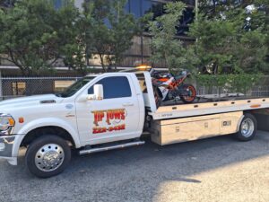 A white Tip Tows flatbed tow truck transporting a motorcycle in Honolulu, HI.