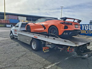 A white Tip Tows flatbed tow truck transporting an orange sports car in Honolulu, HI.