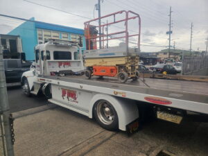 A white Tip Tows flatbed tow truck transporting a scissor lift for equipment towing in Honolulu, HI.