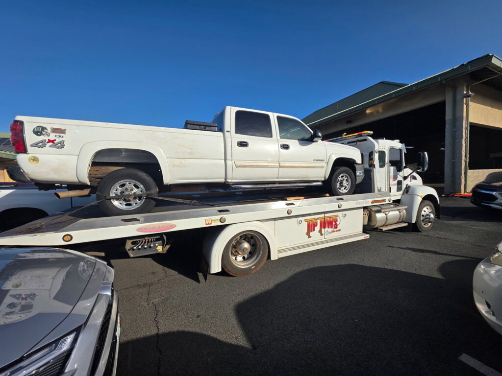 A white Tip Tows flatbed tow truck transporting a white pickup truck in Honolulu, HI.