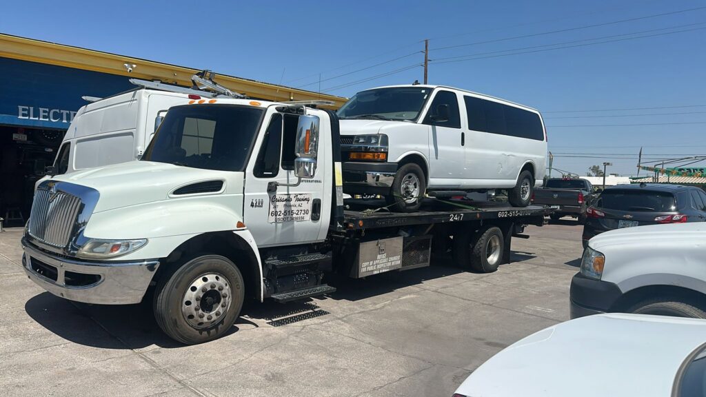 A white Ford F-250 pickup truck being transported on a flatbed tow truck by Crisanto Towing in Phoenix, AZ.