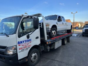 A white Ford F-350 dually pickup truck on a flatbed tow truck with the Anytime towing services logo in Columbus, OH.