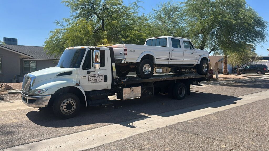 A white Ford pickup truck being transported on a flatbed tow truck by Crisanto Towing in Phoenix, AZ.