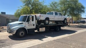 A white Ford pickup truck being transported on a flatbed tow truck by Crisanto Towing in Phoenix, AZ.