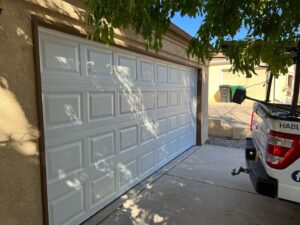 A white panel garage door on a residential home, serviced by Excellence Garage Doors LLC in Albuquerque, NM, with their truck parked nearby.