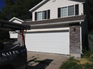 A white garage door on a house with a service truck from Alpine Overhead Garage Door Service on site in Layton, UT.
