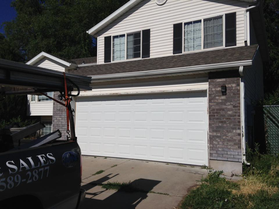 A white garage door on a house with a service truck from Alpine Overhead Garage Door Service on site in Layton, UT.
