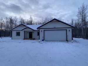 A white garage door installed on a house in a snowy winter setting by Elite Doors in Wasilla, AK.