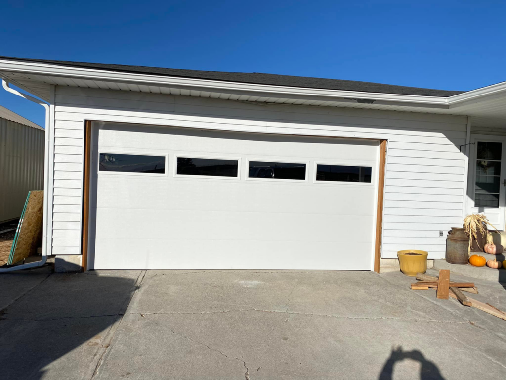 A new white garage door with horizontal windows installed on a residential home by MBP Garage Doors in Firth, ID