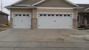 White garage doors with decorative hardware and windows on a new home by Cedar Valley Garage Doors in Waterloo, IA