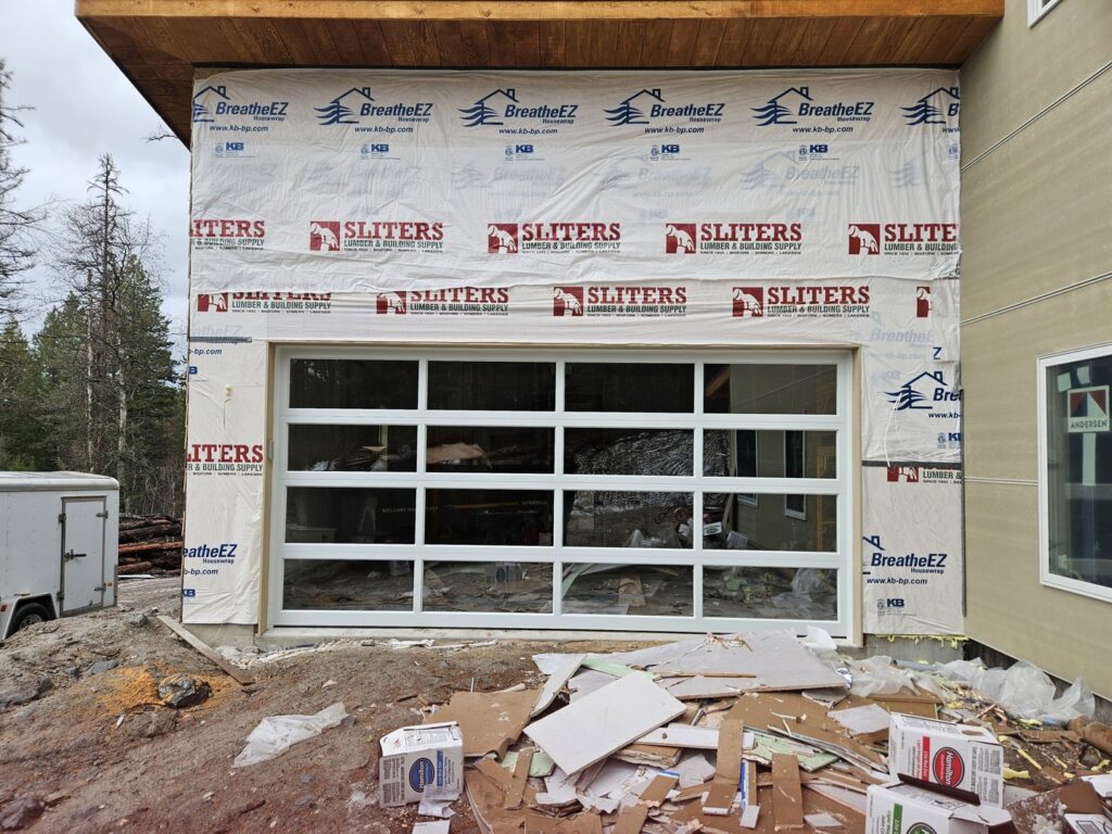 A white glass garage door installed on a building under construction, with debris, by Riverside Garage Doors in Kalispell, MT.