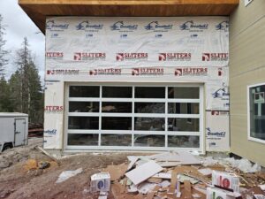 A white glass garage door installed on a building under construction, with debris, by Riverside Garage Doors in Kalispell, MT.
