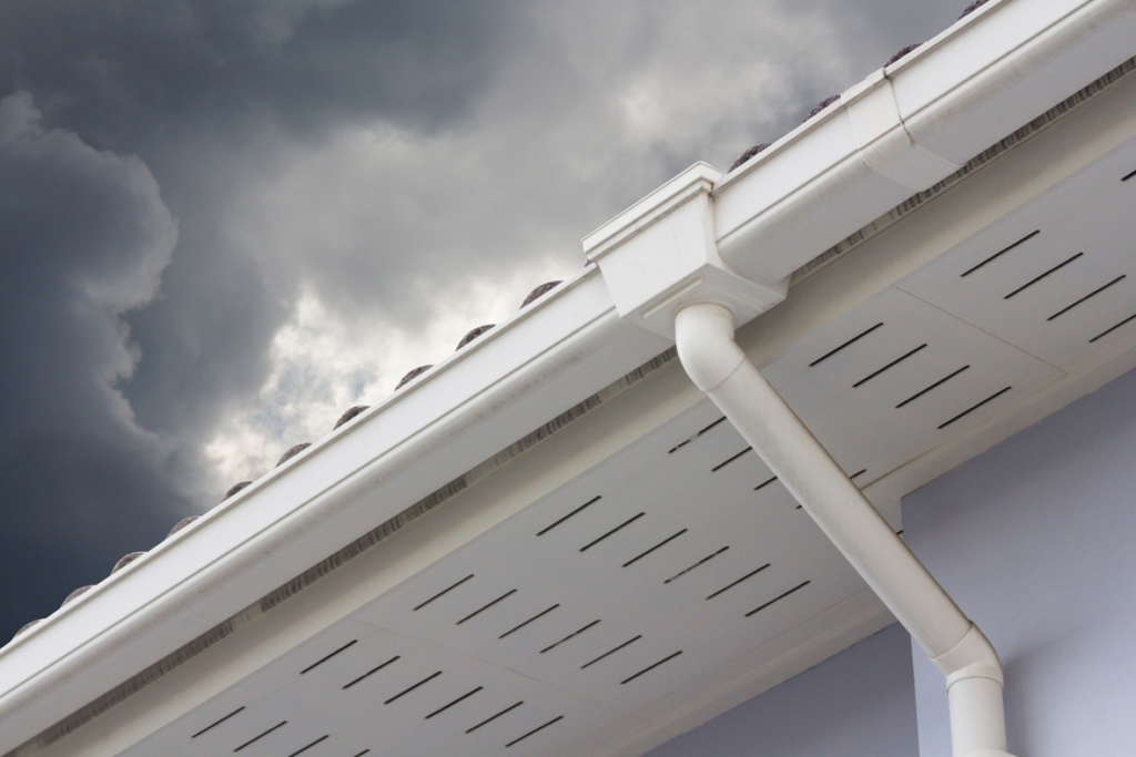 A white gutter and downspout on a house under a stormy sky, managed by Papillion Windows & Siding - NE in Papillion, NE.