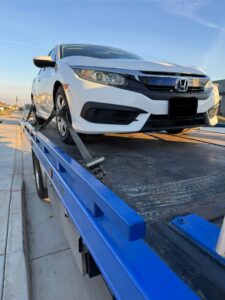 A white Honda Civic securely loaded onto a blue flatbed tow truck by A&A Towing Services in Bakersfield, CA.