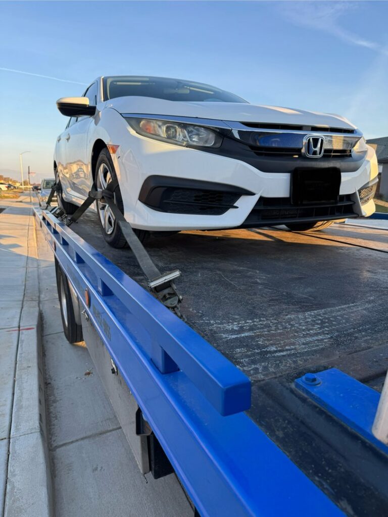 A white Honda Civic securely loaded onto a blue flatbed tow truck by A&A Towing Services in Bakersfield, CA.