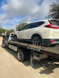 A white Honda CR-V being transported on a flatbed tow truck by Jay Towing Services in Houston, TX.