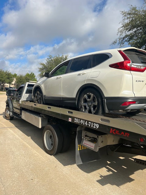 A white Honda CR-V being transported on a flatbed tow truck by Jay Towing Services in Houston, TX.