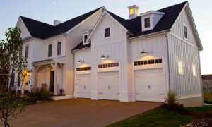 A beautiful white house featuring three classic white garage doors with windows installed by Standard Door Supply in Portland, ME.
