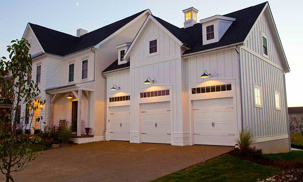 A beautiful white house featuring three classic white garage doors with windows installed by Standard Door Supply in Portland, ME.