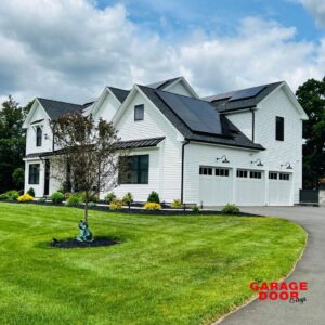 A white house with two white panel garage doors and solar panels, installed by The Garage Door Guys, LLC in New Haven, CT.