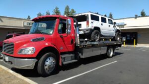 A white Hummer H2 SUV being towed on a flatbed truck in a parking lot by 101 auto towing inc in San Jose, CA.