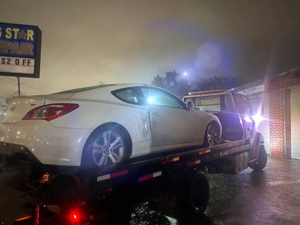A damaged white Hyundai Genesis coupe being loaded onto a flatbed tow truck at night by Towing Near Me 247 LLC in Irving, TX.