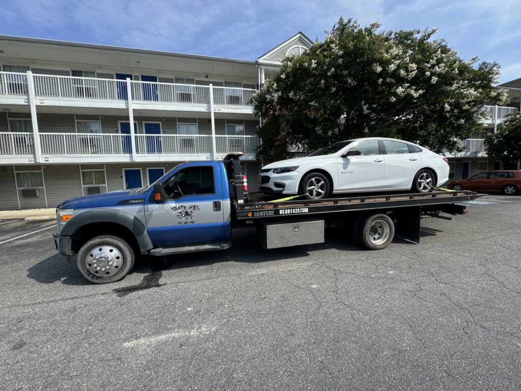 A white Infiniti sedan being transported on a flatbed tow truck by Hampton Roads Towing Services in Chesapeake, VA.
