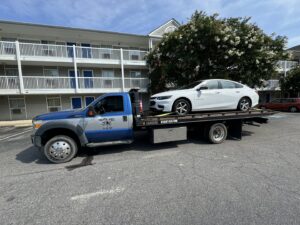 A white Infiniti sedan being transported on a flatbed tow truck by Hampton Roads Towing Services in Chesapeake, VA.