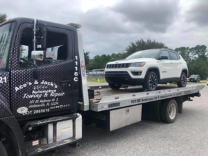 A white Jeep Compass SUV being towed on a flatbed truck by Aces & Jacks Automotive in Jacksonville, FL.