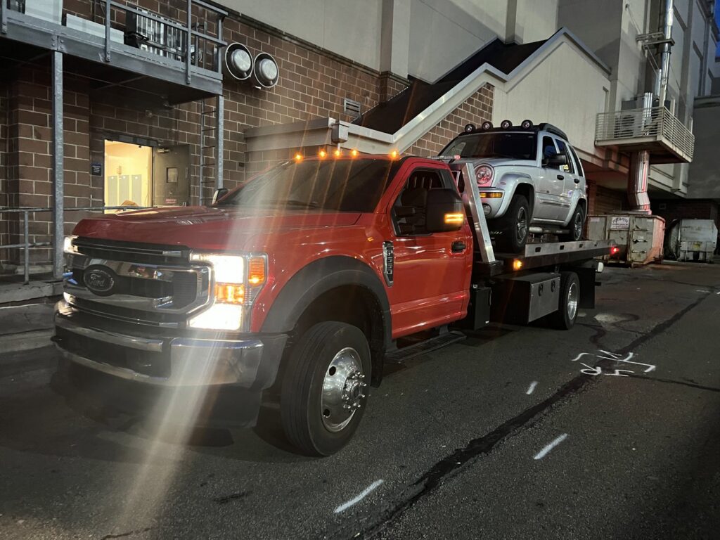 A white Jeep Liberty being transported on a flatbed tow truck by Quiñones Towing in Cleveland, OH.