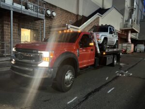 A white Jeep Liberty being transported on a flatbed tow truck by Quiñones Towing in Cleveland, OH.