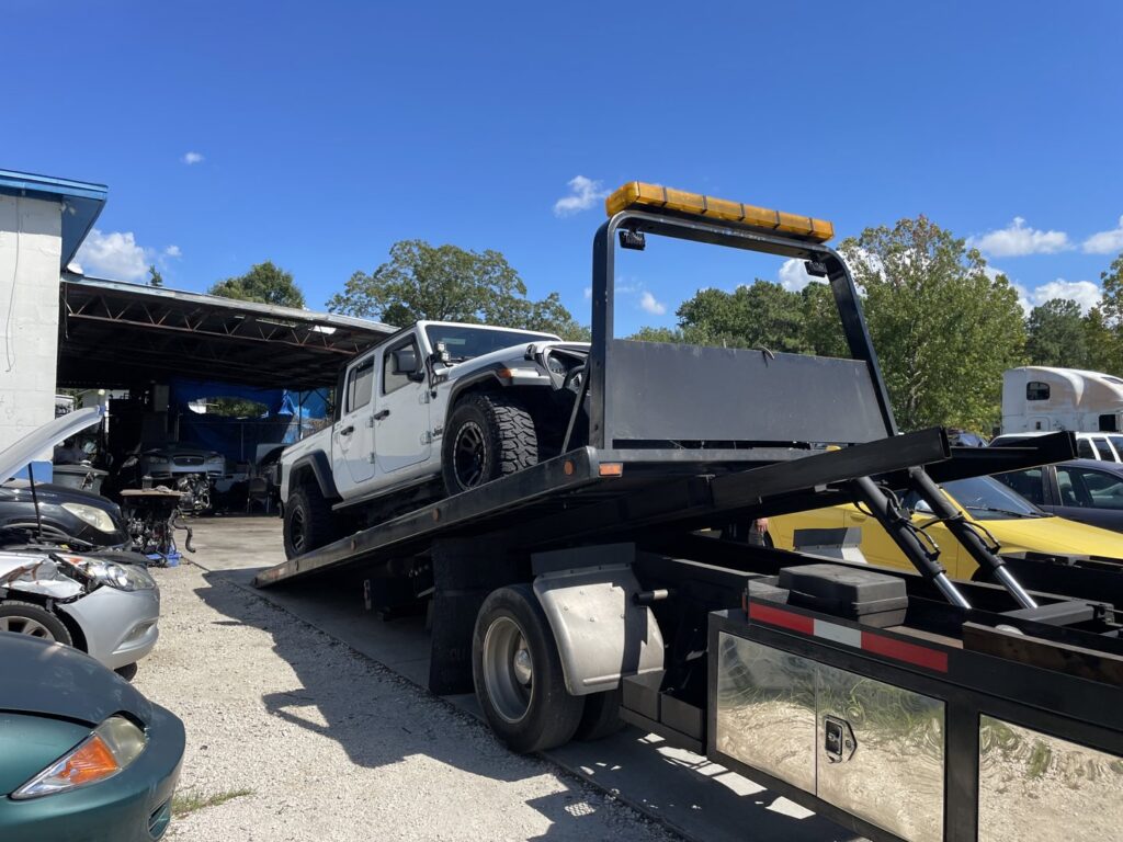 A white Jeep pickup truck being loaded onto a flatbed tow truck by Tiki's Towing LLC in Jacksonville, FL.
