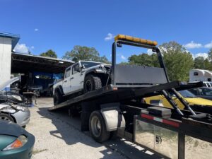 A white Jeep pickup truck being loaded onto a flatbed tow truck by Tiki's Towing LLC in Jacksonville, FL.