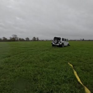 A white Jeep stuck in a grassy field, awaiting recovery by Columbus Towing in Columbus, GA.