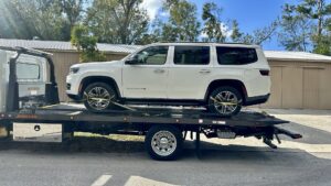 A white Jeep Wagoneer SUV securely loaded onto a TP Towing flatbed truck for transport in Tampa, FL.
