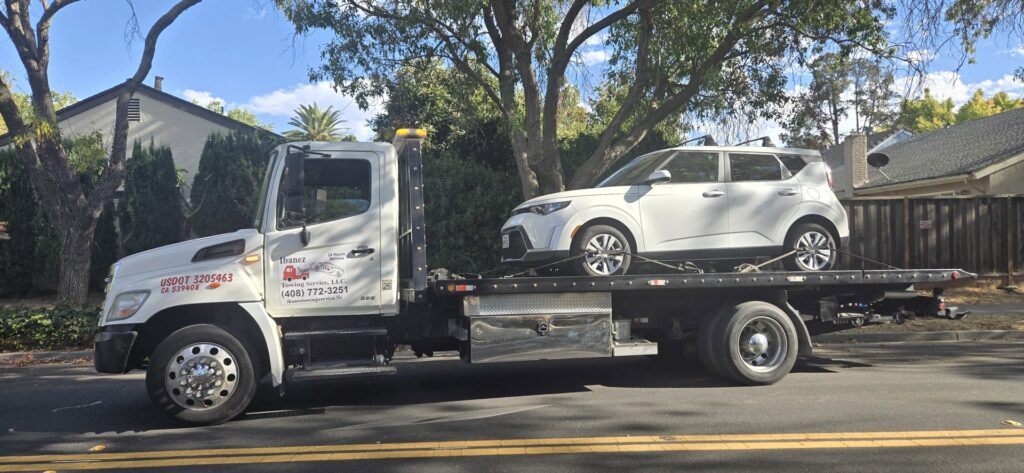 A white Kia Soul being towed on a flatbed tow truck by Ibanez Towing Service LLC in San Jose, CA.