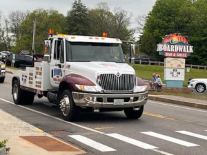 A white and maroon flatbed tow truck from Bailey's Towing and Auto Body, LLC driving on a street in Merrimack, NH.
