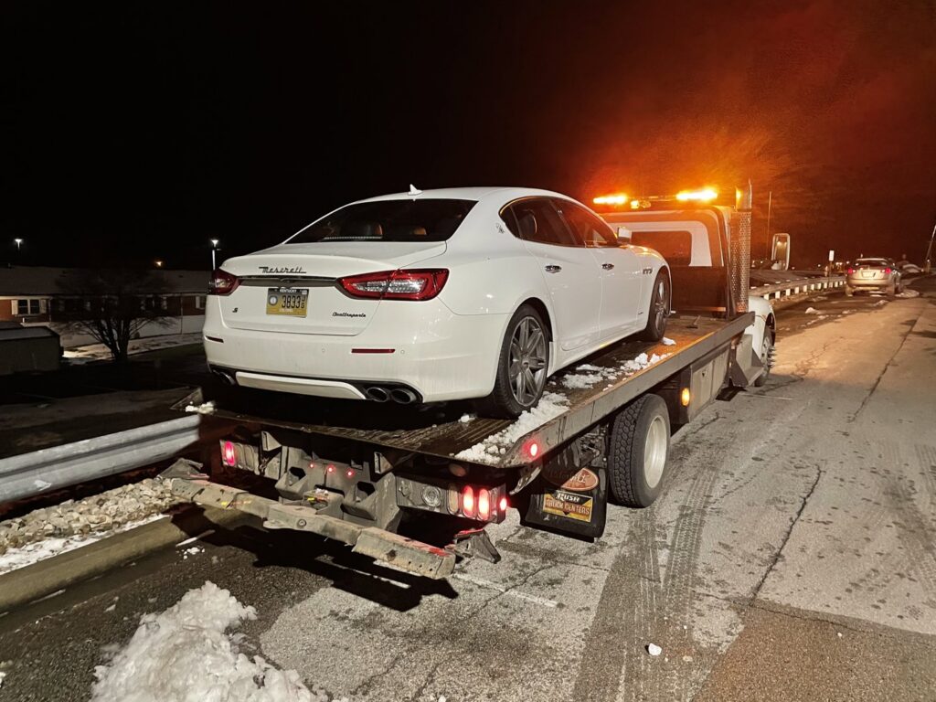 A white Maserati luxury sedan loaded onto a flatbed tow truck from Wilkerson's Towing & Automotive LLC at night in Bowling Green, KY.