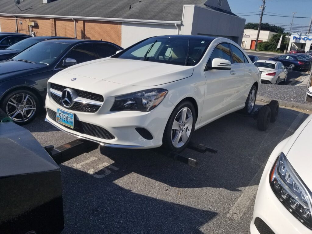 A white Mercedes-Benz sedan being towed by Whitelock Towing in Baltimore, MD, with a tow dolly.