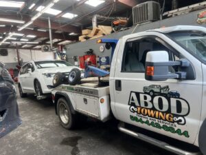 A white minivan being towed by a wheel lift tow truck from ABOD Towing LLC in New Orleans, LA, inside a repair shop.