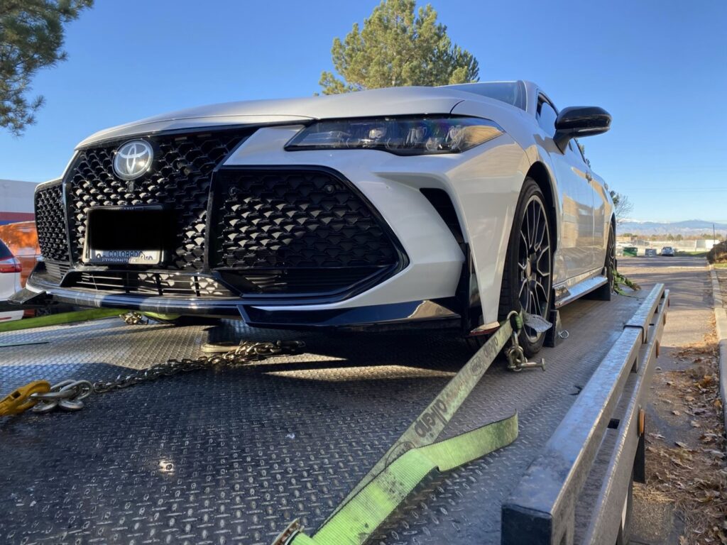 A white modern sedan securely strapped onto a flatbed tow truck by Black Mamba Towing & Recovery Llc in Aurora, CO.
